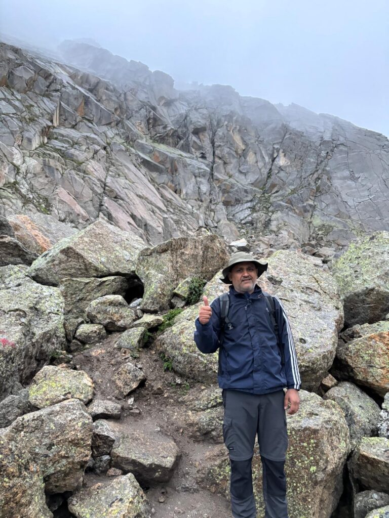 Trekker climbing boulders towards Kinner Kailash peak in fog